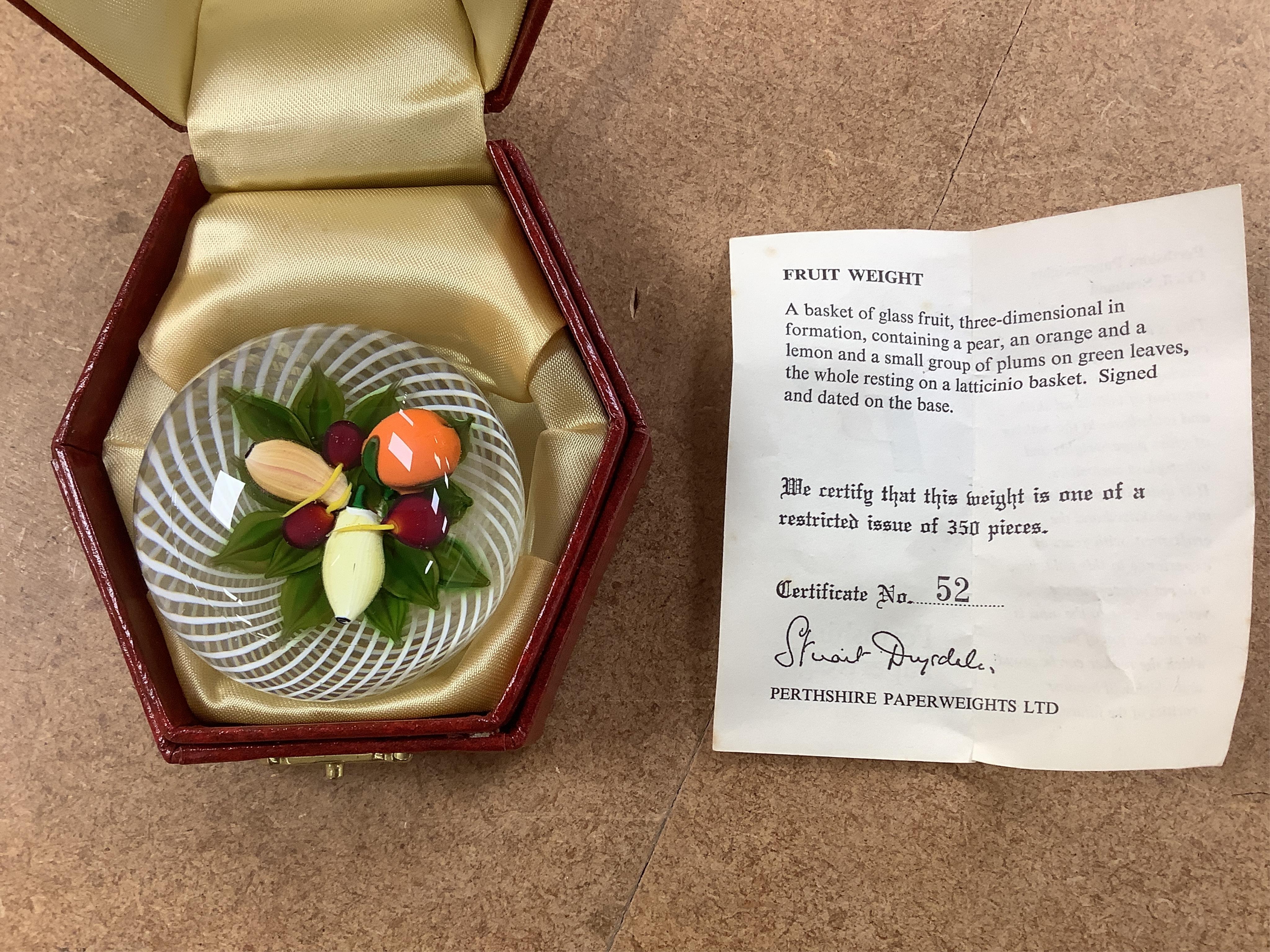 Two Perthshire lamp work glass paperweights, fruit weight, 52/350, rose and bud weight, 69/300 together with a John Deacons bouquet on a ruby base paperweight, edition of 101 (3)